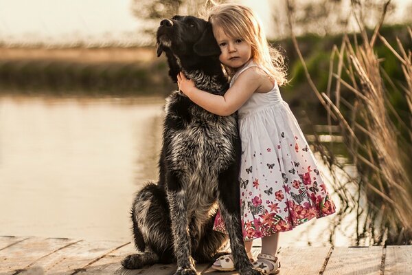 Una niña y un perro caminan cerca del río