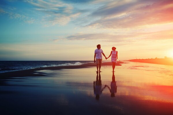 A couple walks along the seashore at sunset