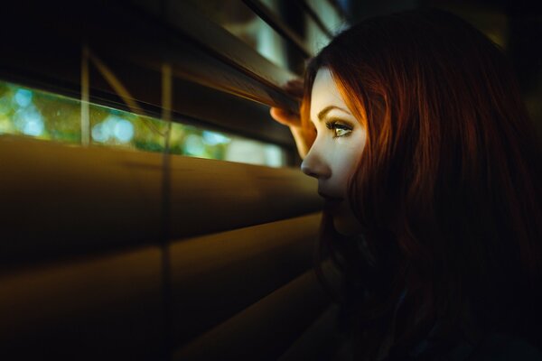 The girl looks at the street through the blinds