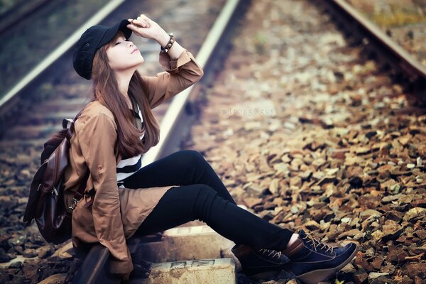 An Asian girl in a cap is sitting on the railway tracks