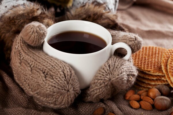 Café en una taza abraza las manos en mitones