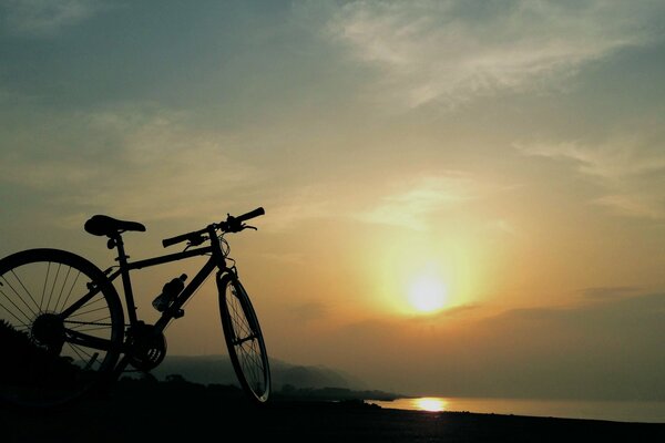 The bike is on the shore of the lake at sunset