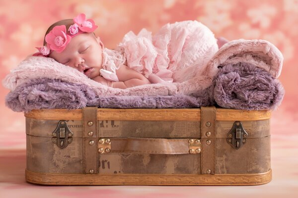 A baby with a wreath on his head sleeps on a suitcase