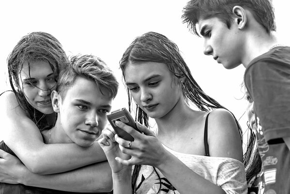 Due ragazzi e due ragazze bagnate guardando con entusiasmo il telefono