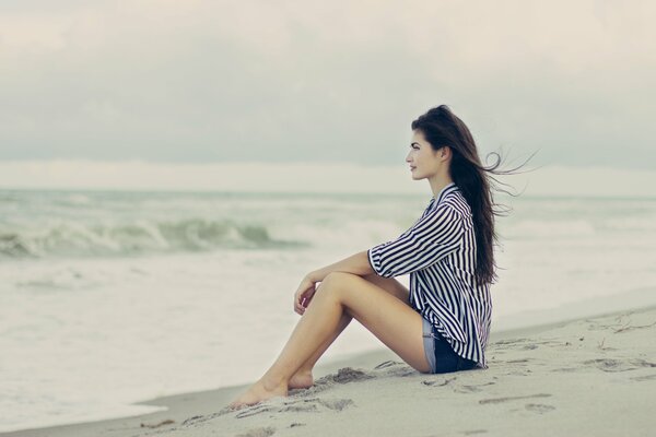 Das Mädchen sitzt auf dem Sand und schaut auf das Meer