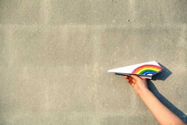 Papierflieger mit Regenbogenflügel auf weißem Wandhintergrund