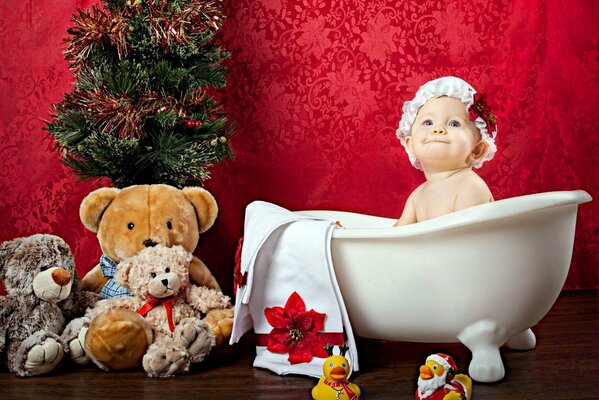 Das Baby in der Mütze sitzt in der Wanne, umgeben von Spielzeug