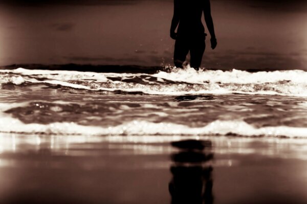 Weibliche Silhouette, die im Meer vor dem Hintergrund des Abendstrandes und der Wellen liegt