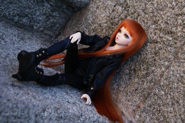 A doll with long red hair sits on a rock