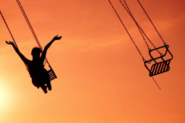 A girl on an attraction with her hands raised against the sunset