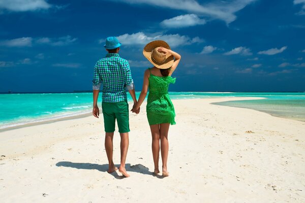 In the tropics, a couple walks on the beach among palm trees