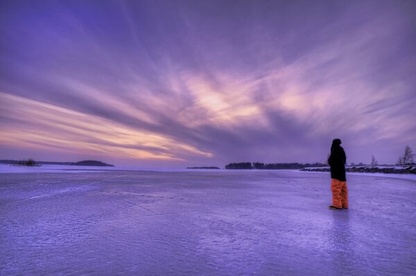 Ein Mann auf dem Eis bewundert den lila Himmel in Schweden