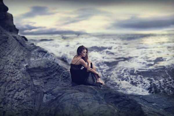 Chica triste sentada en una roca junto al mar