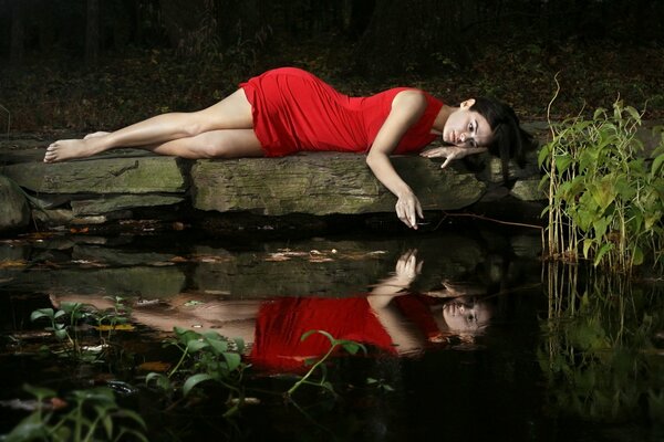 The girl in red on the stone by the lake is sad