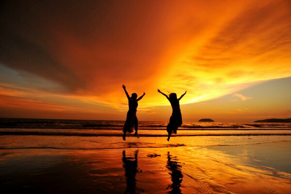 Two girls at sunset on the seashore jump in delight and joy