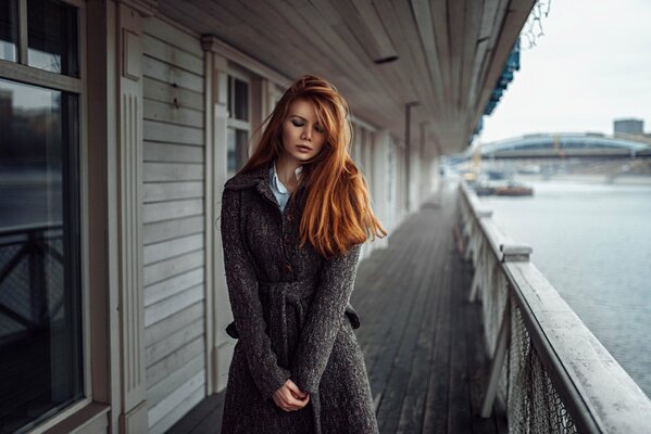 A girl with red hair is standing on the shore behind the fence