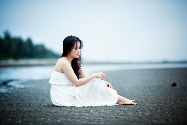 A girl in white is sitting on a deserted shore