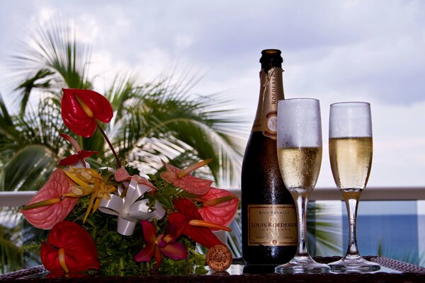 A bouquet of flowers next to two glasses and a bottle of champagne