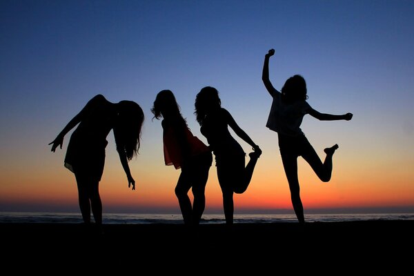 Silhouettes of girls by the sea against the sunset