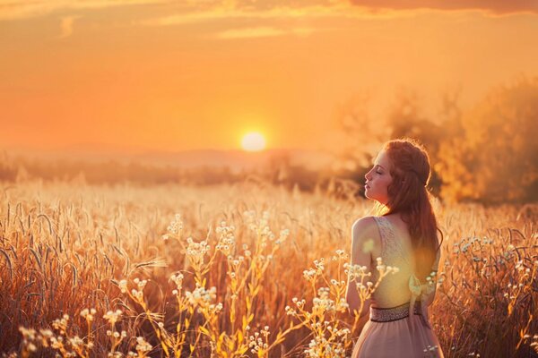 Red-haired girl against the background of the sun in the field