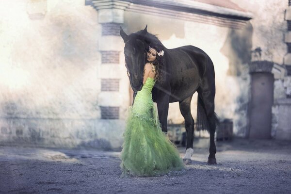 La ragazza bruna in un vestito verde lussureggiante con un fiore nei capelli abbraccia il cavallo