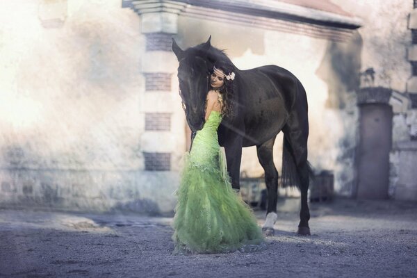 Девушка брюнетка в пышном зелёном платье с цветком в волосах обнимает лошадь