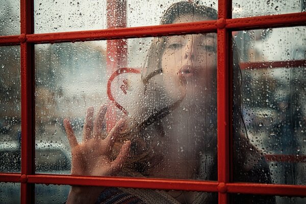 A girl draws a heart on a fogged window