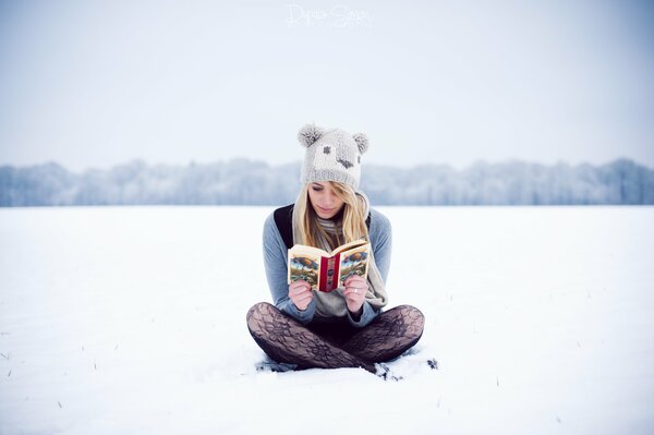 Mädchen mit Mütze liest ein Buch im Schnee