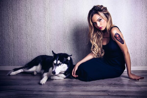 Fille avec un tatouage assis avec un chien Husky sur un mur de fond Uni