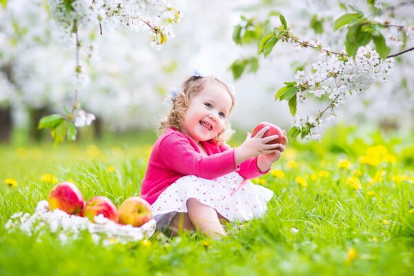 Радостный ребенок с яблоком в руках сидит на траве