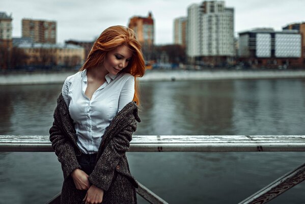 Pelirroja chica en el puente en el fondo de la ciudad