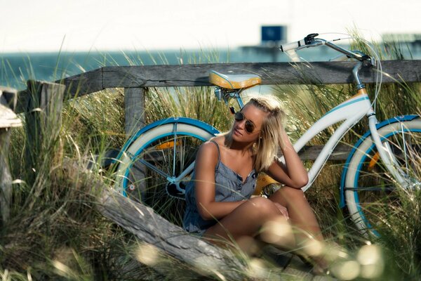 Девушка сидит у велосипеда на лугу