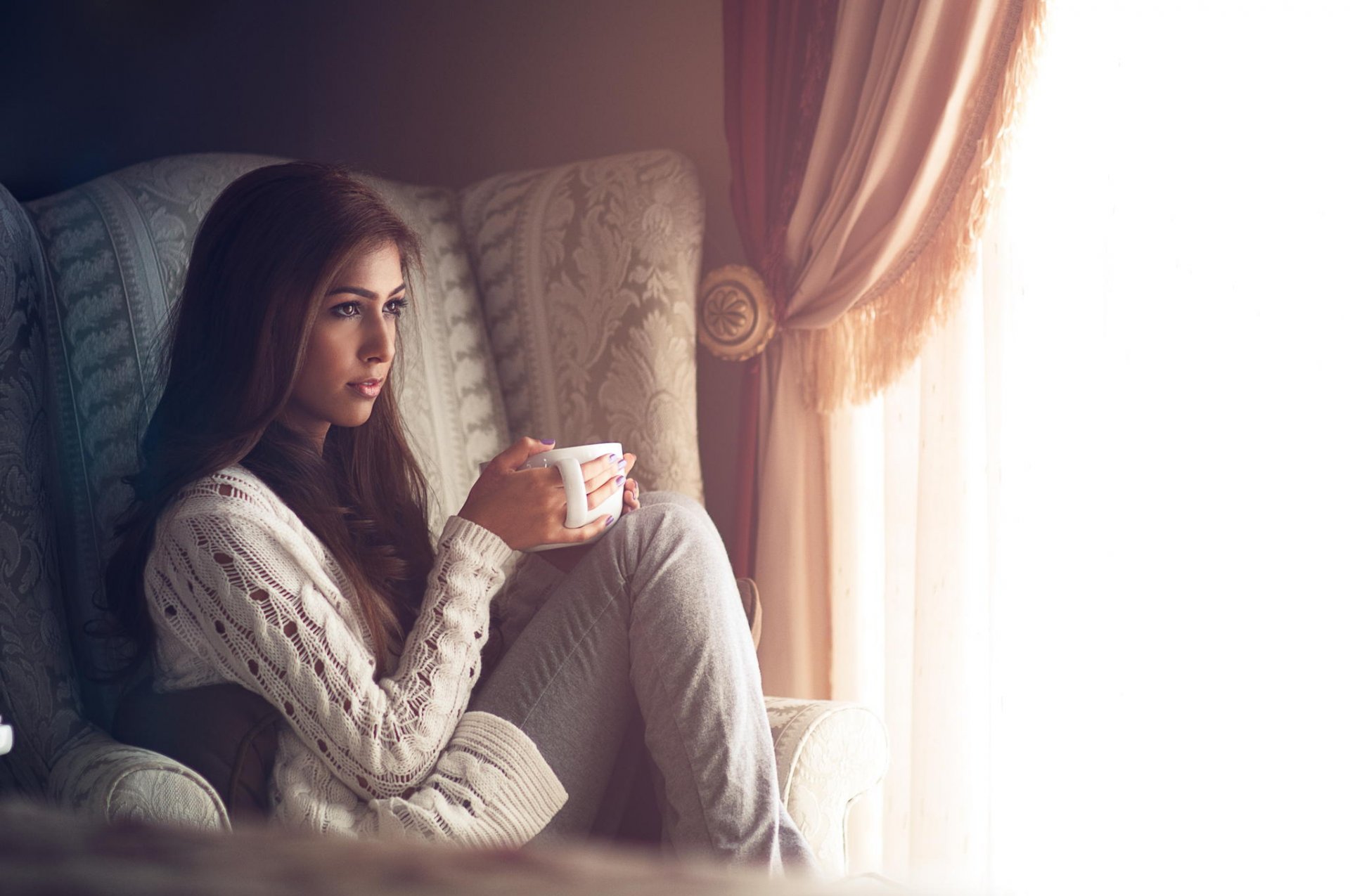 la jeune fille la chambre la fenêtre un fauteuil une tasse le confort rideaux