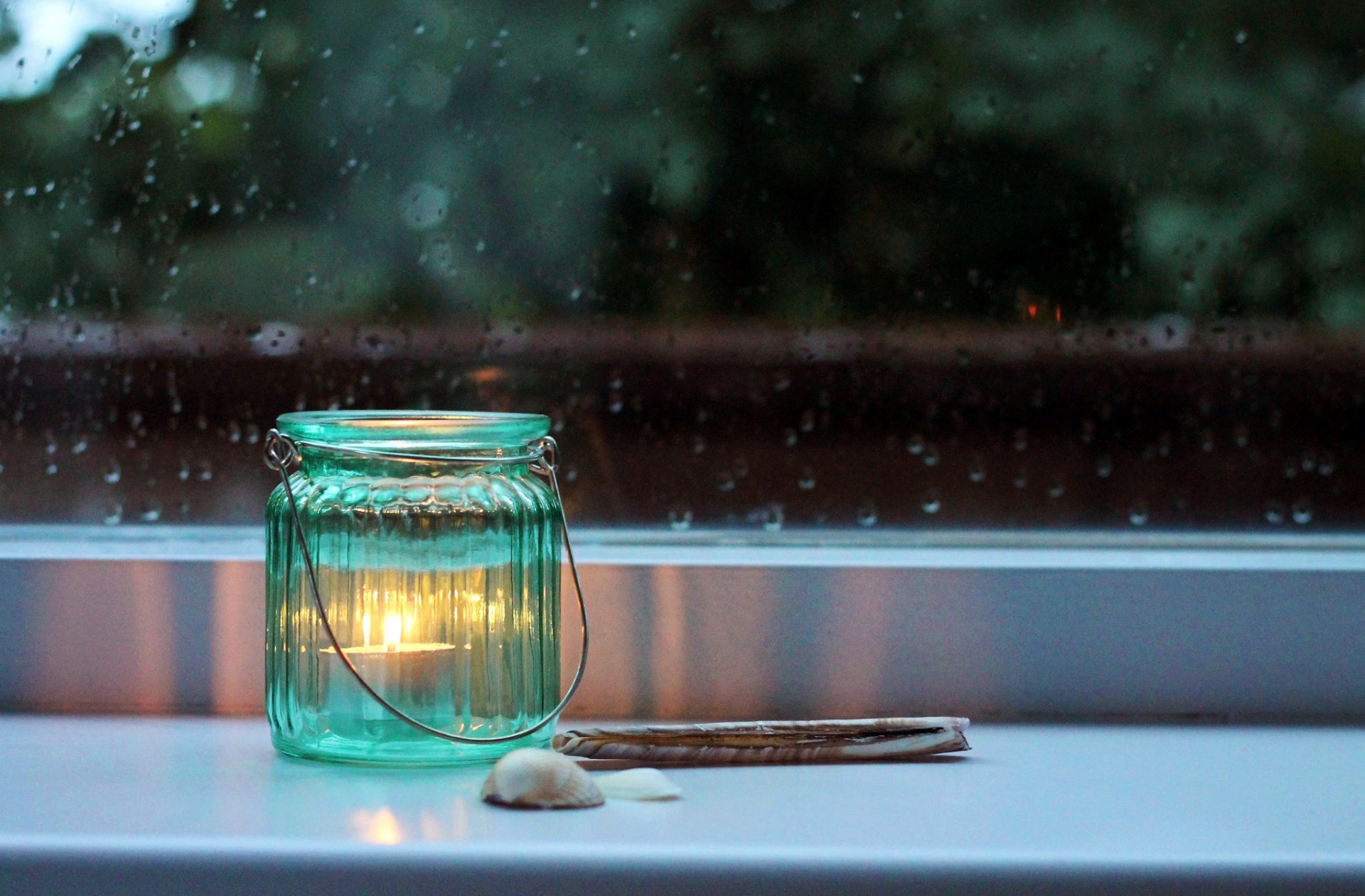 candle jar of the bank shells the window sill window glass rain night