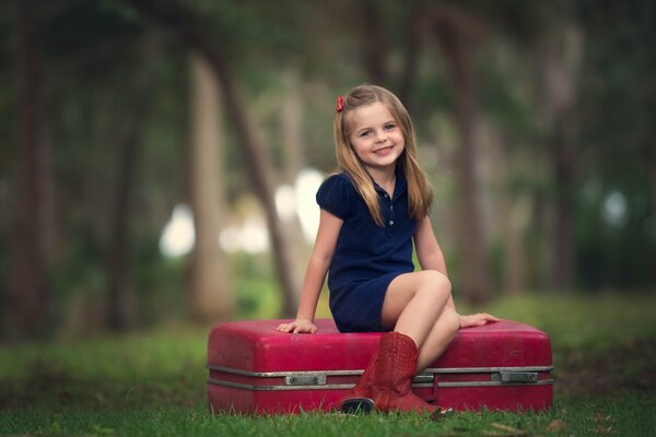 The girl is sitting on a red suitcase