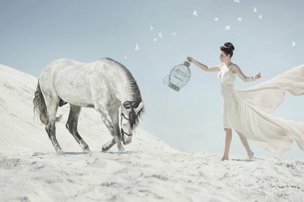 Una donna in un abito bianco volante con una gabbia per uccelli in mano cammina verso un cavallo bianco sullo sfondo del deserto artico