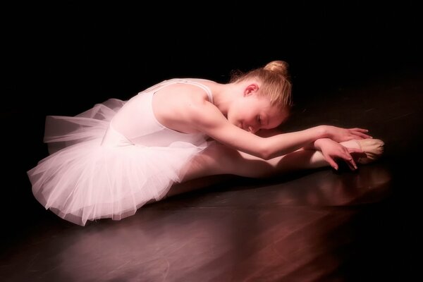 A ballerina girl does stretching in a tutu and pointe shoes
