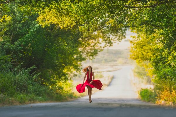 La jeune fille dans une robe rouge va sur la route