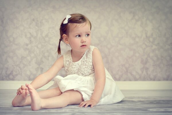 A girl in a white dress is sitting on the floor