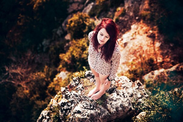 Red-haired girl on a rock barefoot