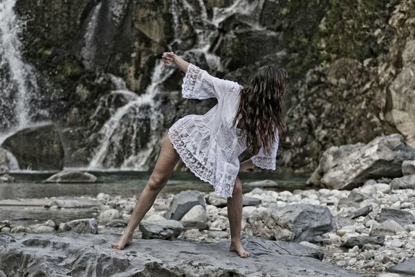 Fille en robe blanche danse sur la rive de la rivière de montagne