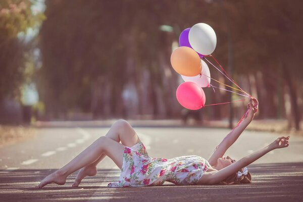 A girl on the road is lying with balloons