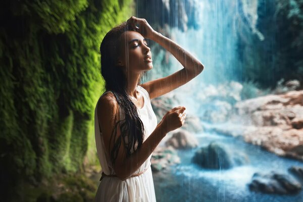 A girl in a dress stands next to a waterfall