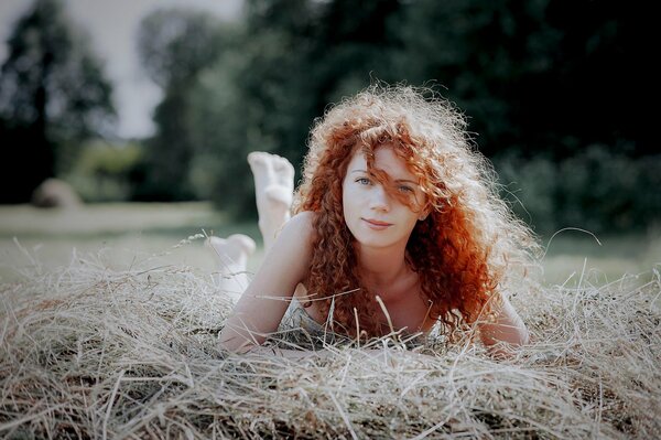 A red-haired girl is lying on a haystack