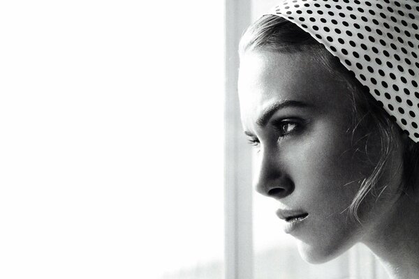 A beautiful woman in a polka dot hat looks out the window