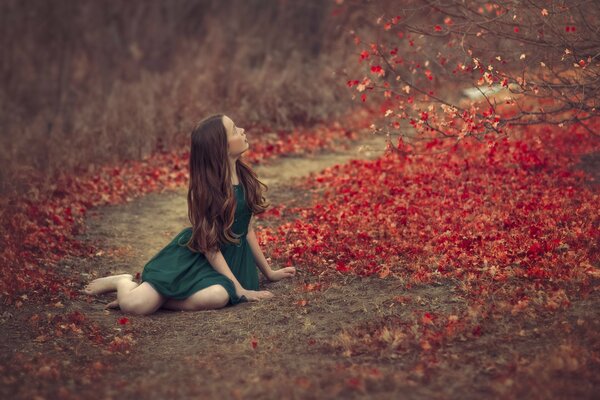 Dziewczyna siedzi na drodze i patrzy na czerwone opadłe liście