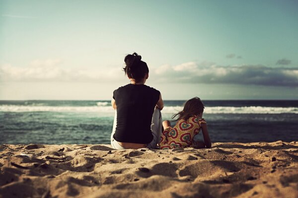 A woman and a girl are sitting on the beach