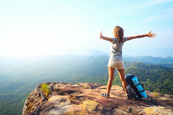 A girl with a backpack at a cliff in the mountains