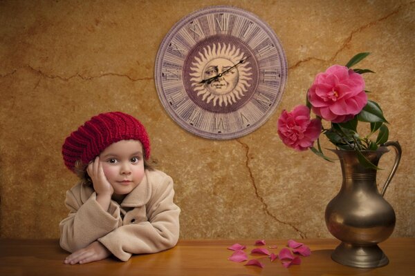 Una niña en una boina rosa se sienta en una mesa con peonías