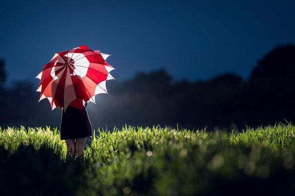 Mädchen mit rot-weißen Regenschirm im Gras in der Nacht